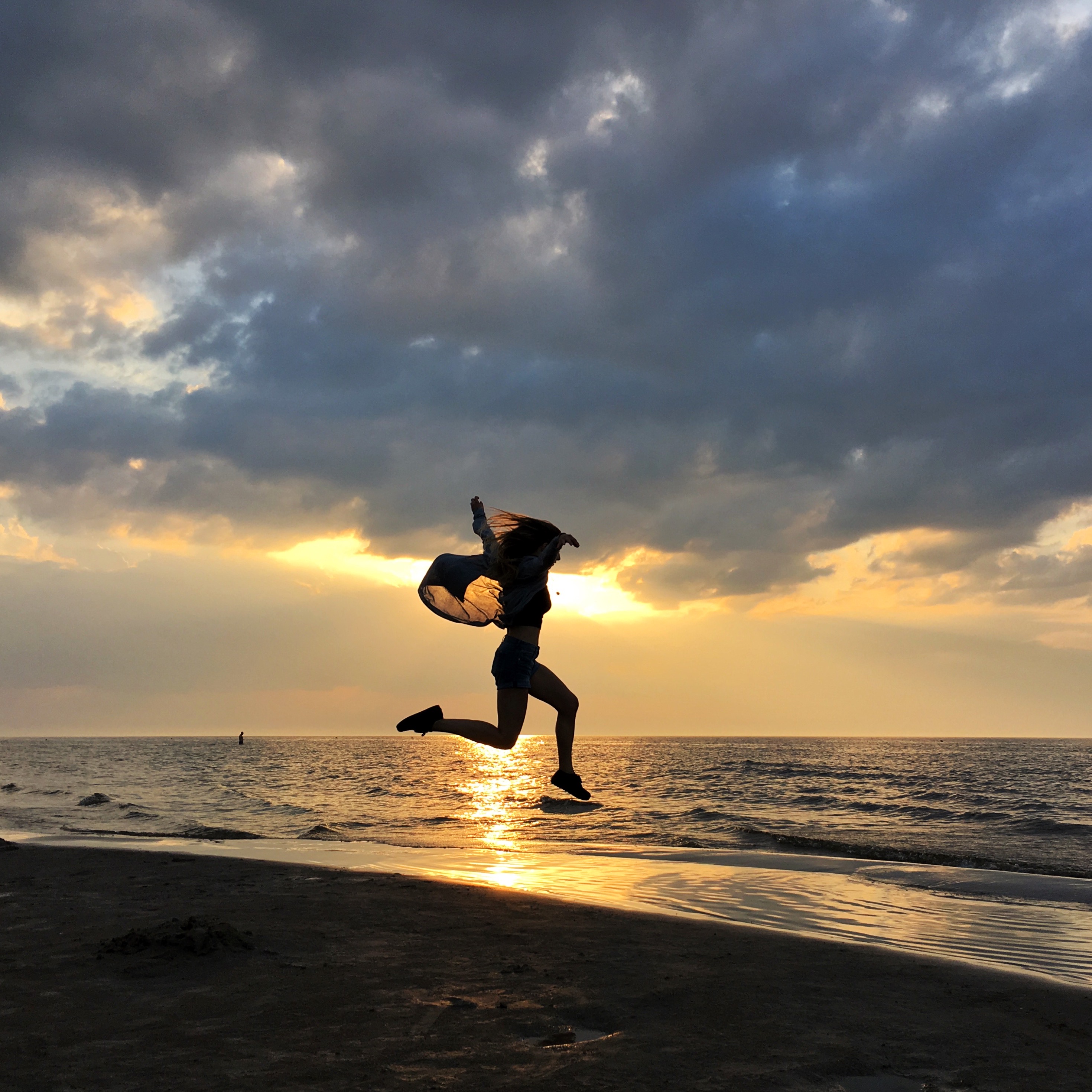 A person silhouetted against a golden sunset, frozen mid-jump on a beach, the kind of split-second action burst mode captures.
