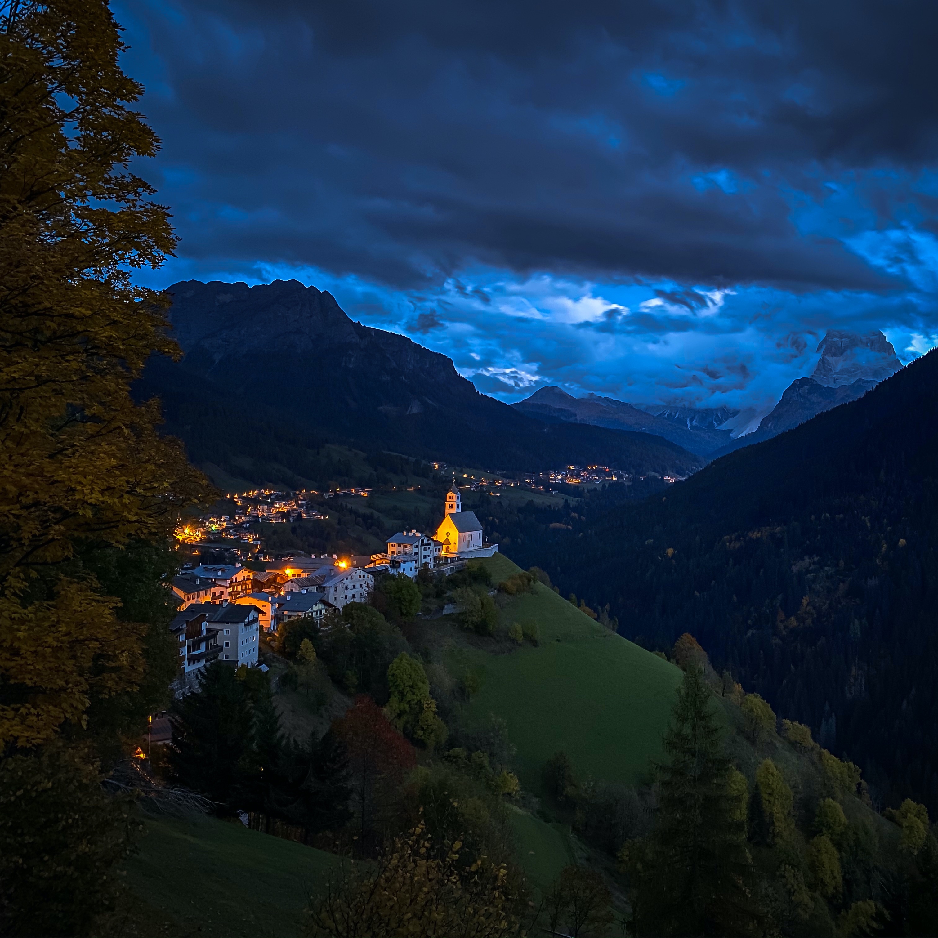 A mountain village glowing under a deep blue twilight sky, captured sharply in low light.