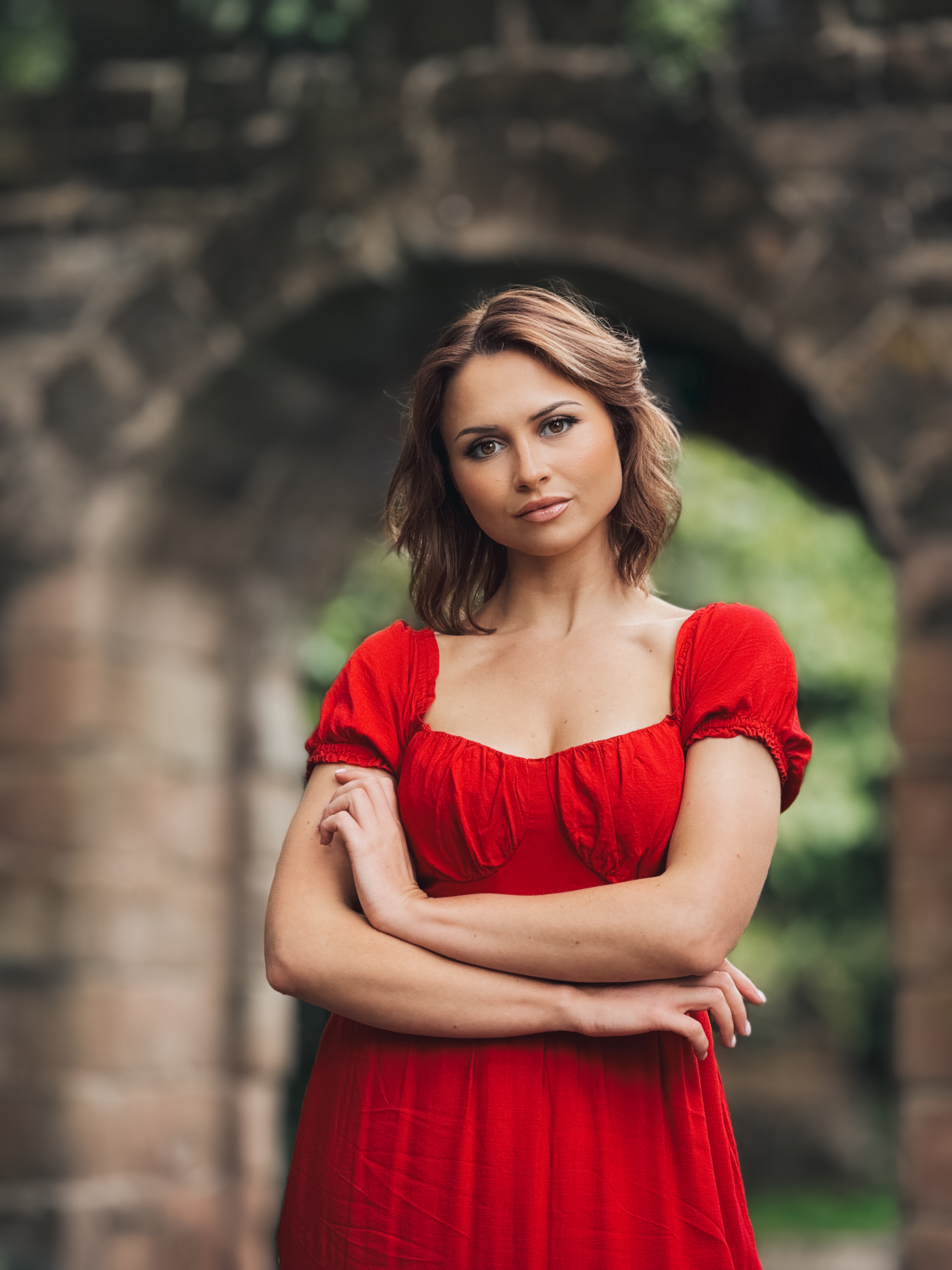 A flattering portrait of a woman in a red dress with a softly blurred stone-arch background.