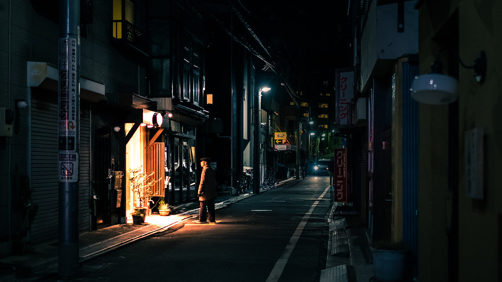 A pedestrian crossing a sunlit city street, caught mid-stride as their shadow stretches across the pavement.