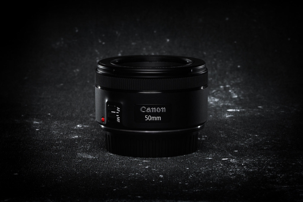 A small prime lens detached from a camera body resting on a textured surface.