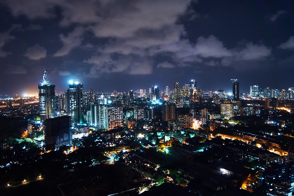 A smartphone held up to capture a dim city street at night, the screen showing a bright, clear image of the scene.