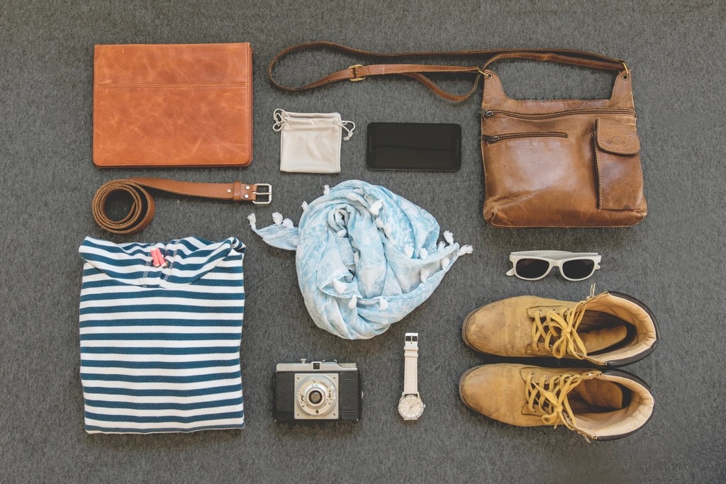 A flat-lay of camera accessories including spare batteries, memory cards, a lens cloth, and a small tripod.
