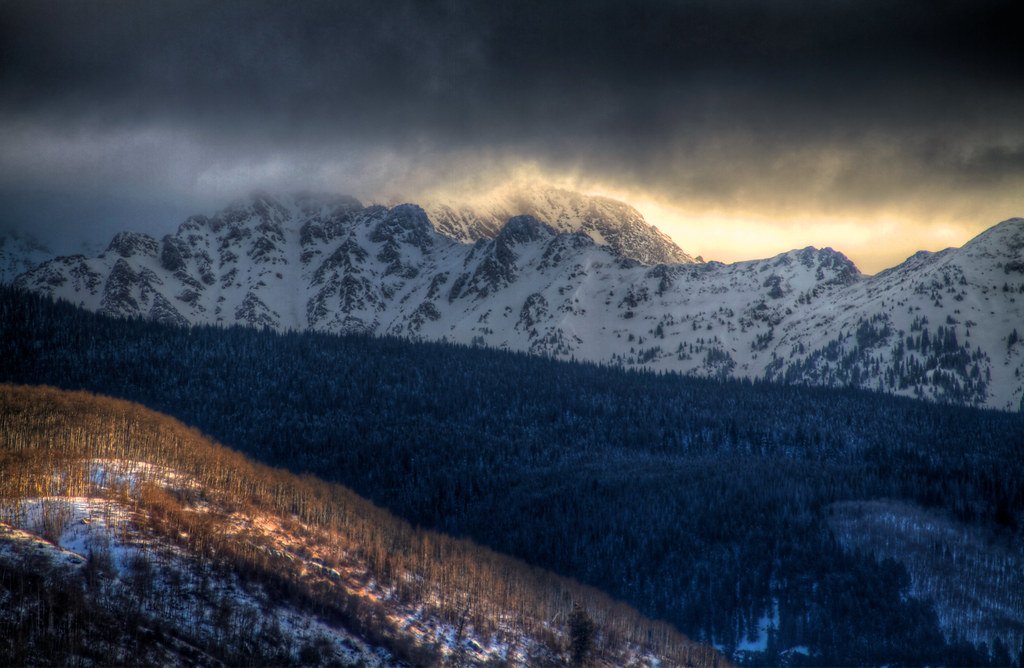 A mountain valley at dawn with a winding river leading the eye from a rocky foreground toward distant peaks.