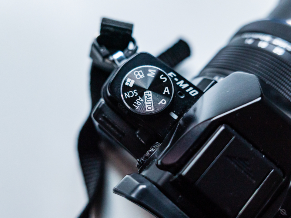 A photographer adjusting settings on a camera held at chest height, dials and buttons in focus.