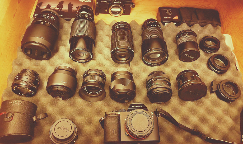 Two camera lenses side by side on a wooden table, one compact prime and one larger zoom.