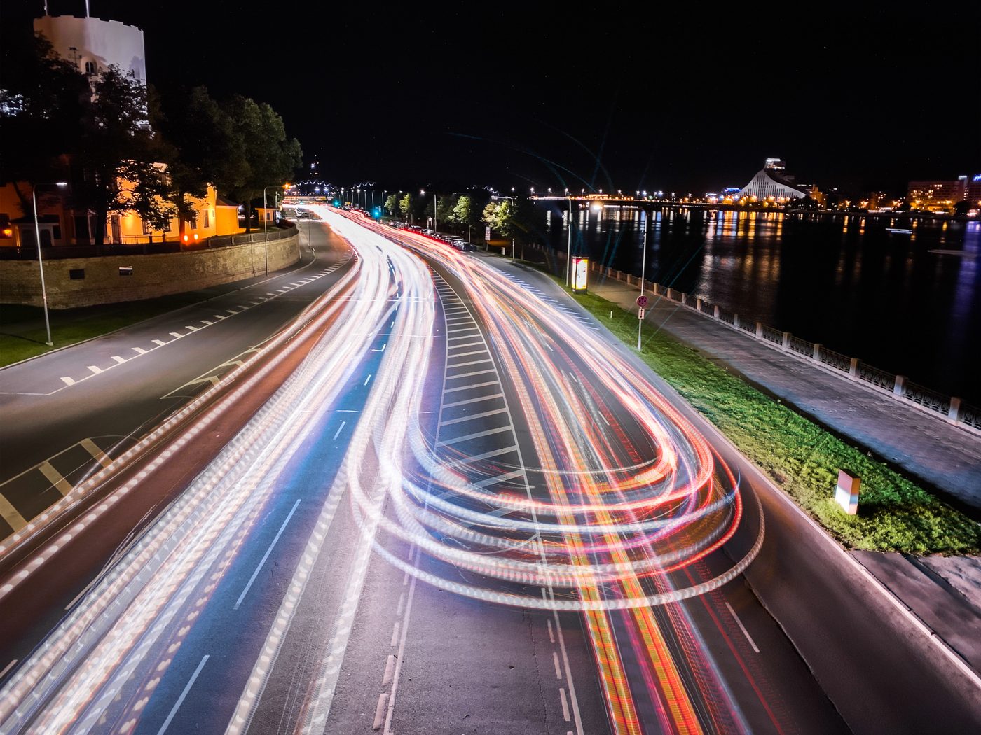 Long ribbons of car lights curving along a riverside road at night.